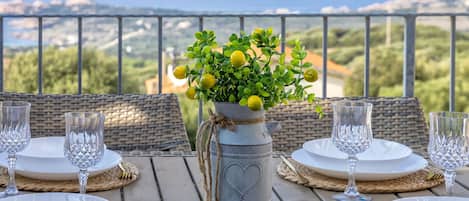 Mesa lista para comer con vista al mar, una planta en maceta y un jarrón decorativo.