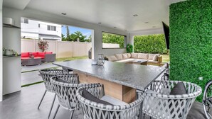 Un espacio moderno al aire libre para comer, con una mesa grande, sillas de mimbre y una pared verde.