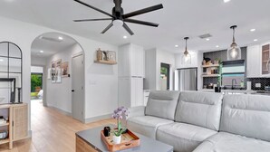 Una sala de estar moderna con un sofá gris, una mesa de centro de madera con una bandeja y un ventilador de techo.