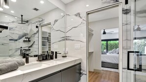 Un baño moderno con salpicadero de mármol, un espejo grande y una ducha a ras de suelo.
