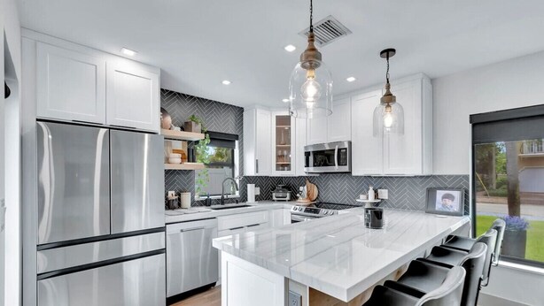 Una cocina moderna con electrodomésticos de acero inoxidable, una isla grande e iluminación colgante.