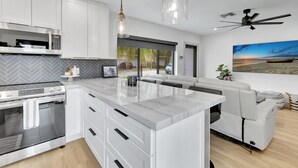 A modern kitchen with white cabinetry, a large island, and a built-in oven. There is a seating area with a sofa and a dining table. - Contemporary 3BR 3 BA Duplex, Amazing Outdoor Area (Fort Lauderdale)