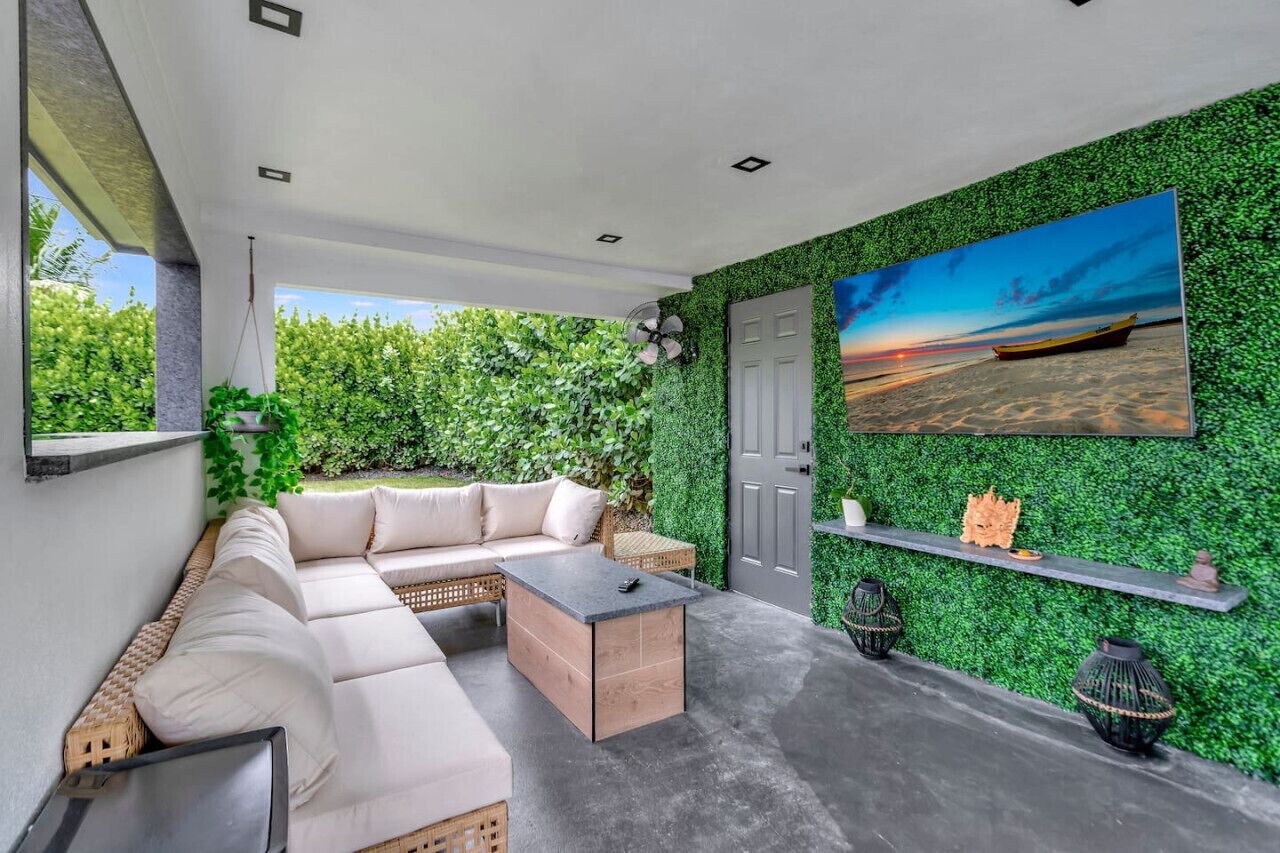 A modern outdoor living space with a sofa, coffee table, and decorative items against a green wall.