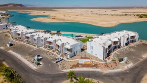 A modern resort with multiple white buildings, a parking area, and a view of a turquoise body of water.