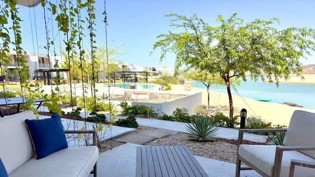 An outdoor seating area with a pool, a tree, and a view of the beach.