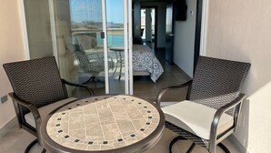 A balcony with two wicker chairs and a round table with a tiled top.
