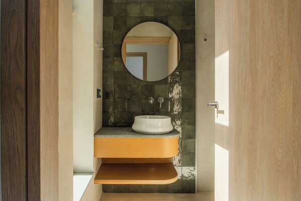 A bathroom with a round mirror, a white sink, and a wooden vanity.