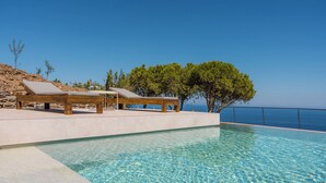 Uma área à beira da piscina com espreguiçadeiras e vista para o mar.