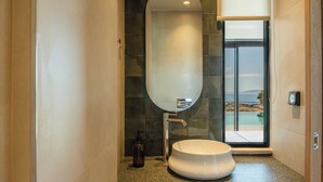 Uma casa de banho moderna com uma pia redonda, um espelho grande e vista para a piscina através de uma porta de vidro.