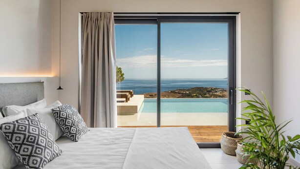 Quarto com cama grande, almofadas estampadas, vista para piscina e oceano, e porta de vidro deslizante.