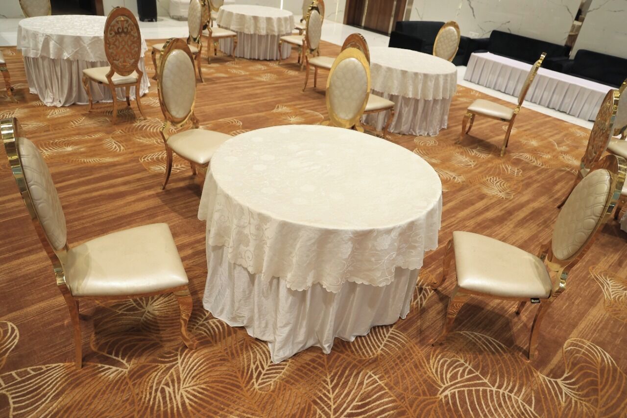 Una sala de conferències amb taules i cadires rodones, terra amb moqueta i tovallons blancs.