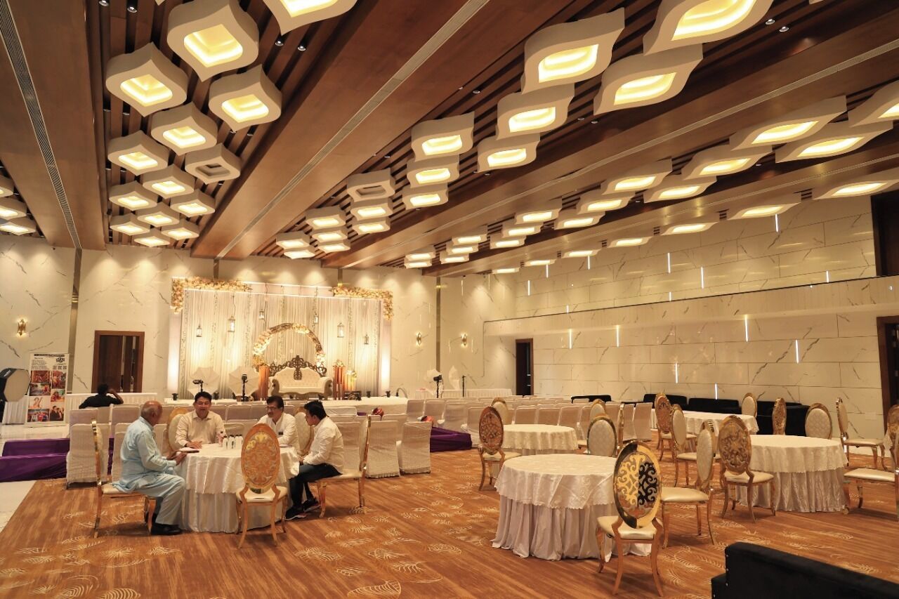 A banquet hall with round tables and chairs, a stage with a floral arrangement, and a ceiling with recessed lighting.