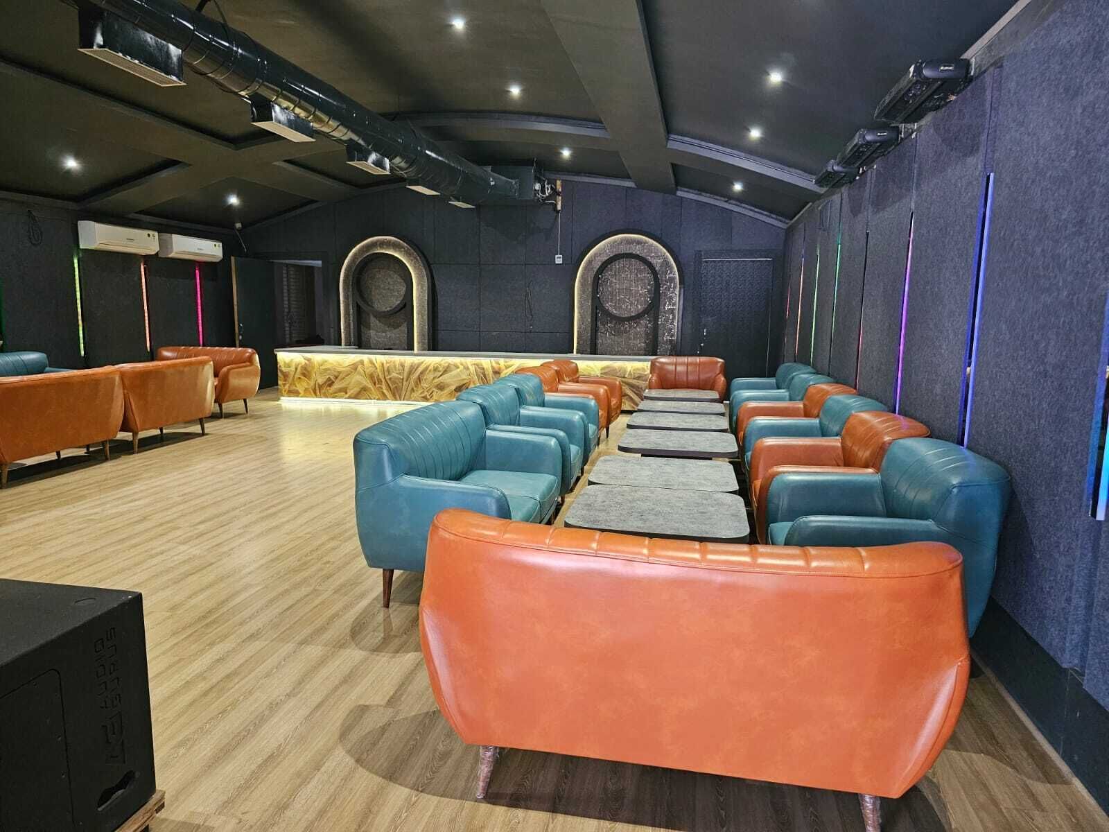 Un cine con filas de asientos de cuero naranja y azul, piso de madera y una pared oscura con diseños circulares.