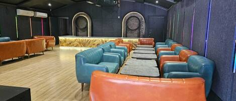 Un cine con filas de asientos de cuero naranja y azul, piso de madera y una pared oscura con diseños circulares.