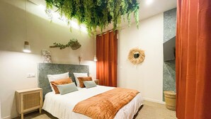 A neatly arranged bedroom with a bed, bedside tables, a hanging plant, and a wall decoration.
