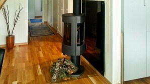 Una habitación con una estufa de leña, piso de madera y una escalera que lleva a otra habitación.