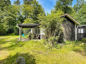 A rustic cabin with a covered patio, surrounded by lush greenery and trees.