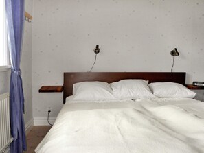 A bedroom with a wooden headboard, a white bedspread, two bedside lamps, and a blue curtain. - 4 Star Holiday Home in Ljung (Ljung)
