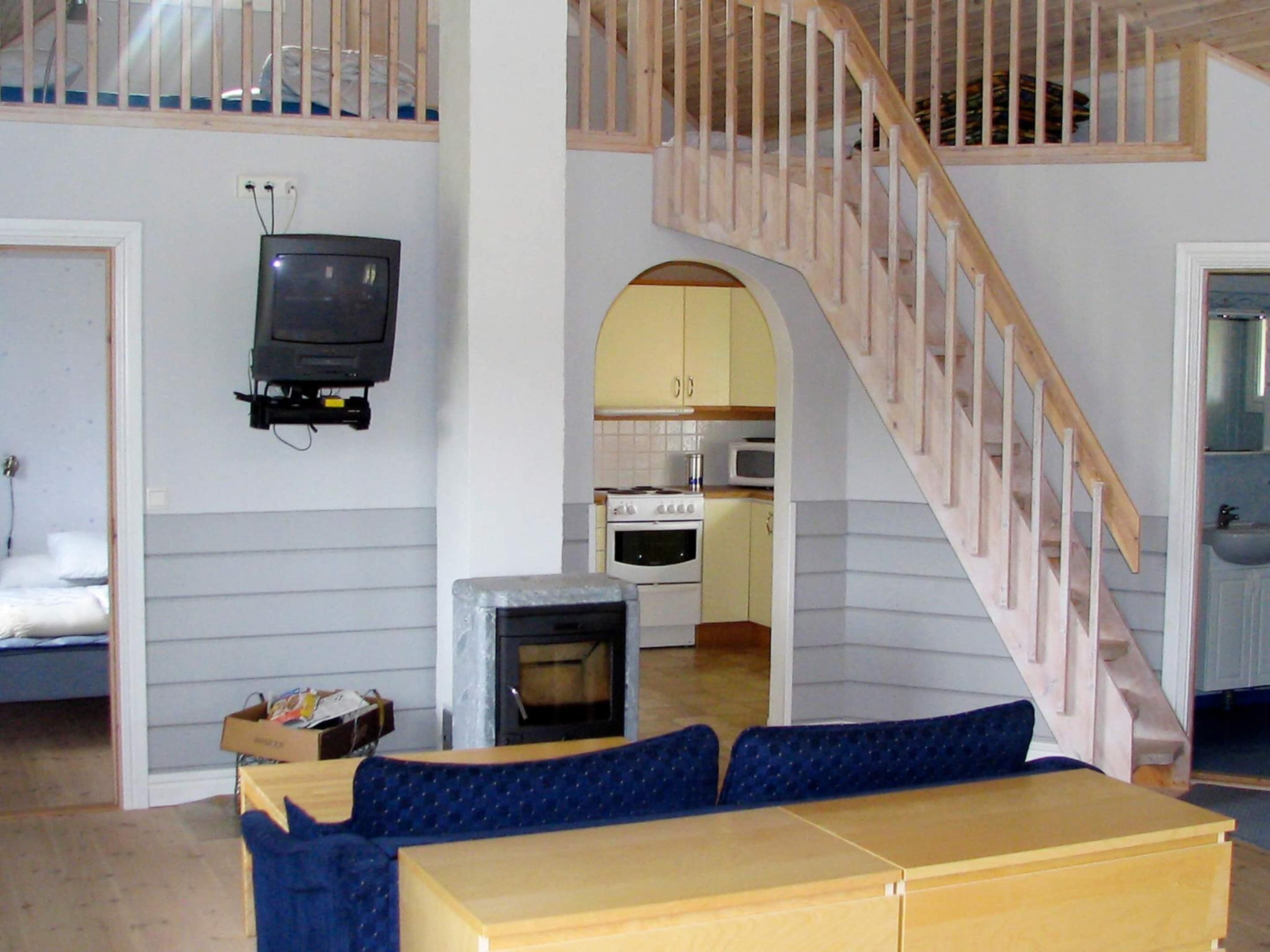 A compact living space with a loft area, a television mounted on the wall, a kitchenette, and a staircase.