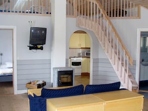 A compact living space with a loft area, a television mounted on the wall, a kitchenette, and a staircase.