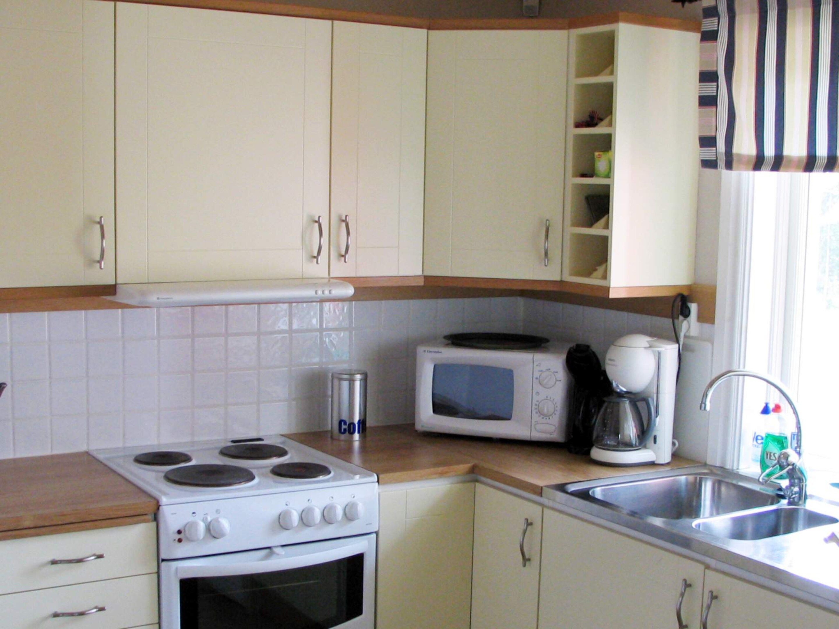 Eine Küche mit weißen Schränken, einem Herd, einem Backofen, einer Mikrowelle, einer Kaffeemaschine und einem Spülbecken.