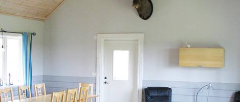 A room with a dining table, chairs, a mounted animal head, a door, and a small table with a lamp.