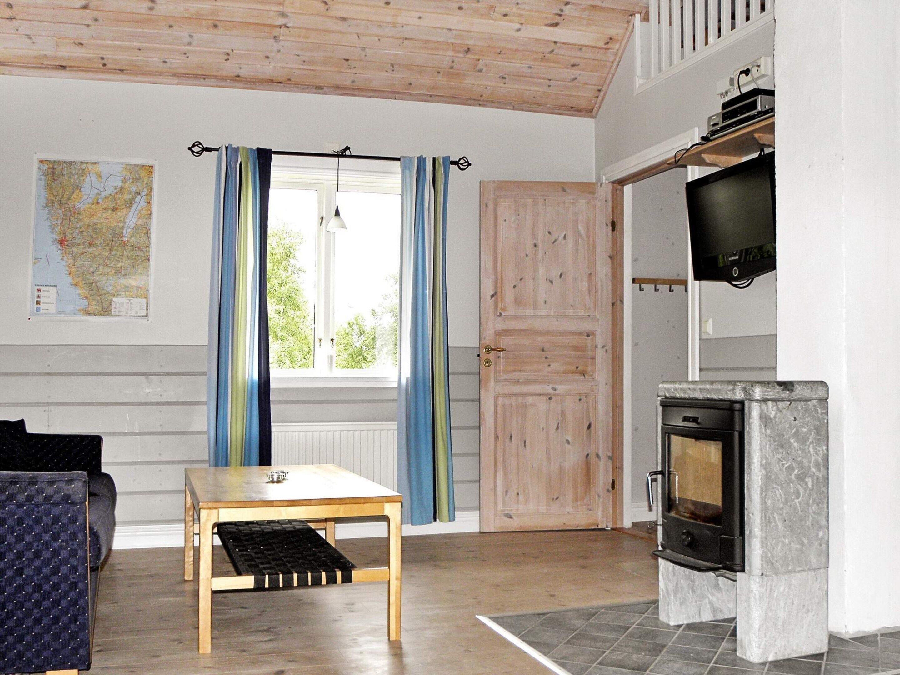 A room with a wooden table, a sofa, a map on the wall, a window with curtains, and a fireplace.