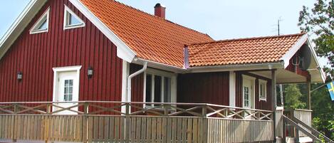 Een rode houten woning met een rode dakbedekking, een veranda en een houten terras.