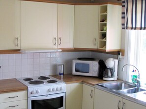 A kitchen with white cabinets, a stove, an oven, a microwave, and a sink. - 4 Star Holiday Home in Ljung (Ljung)