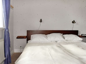 A bedroom with a wooden headboard, two bedside lamps, a white bedspread, and a blue curtain. - 4 Star Holiday Home in Ljung (Ljung)