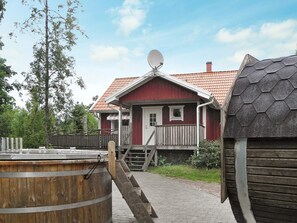 Een rode houten woning met een schotelantenne, een houten terras en een houten vat.