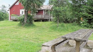 A picnic table in a grassy area with a red building in the background. - 4 Star Holiday Home in Ljung (Ljung)