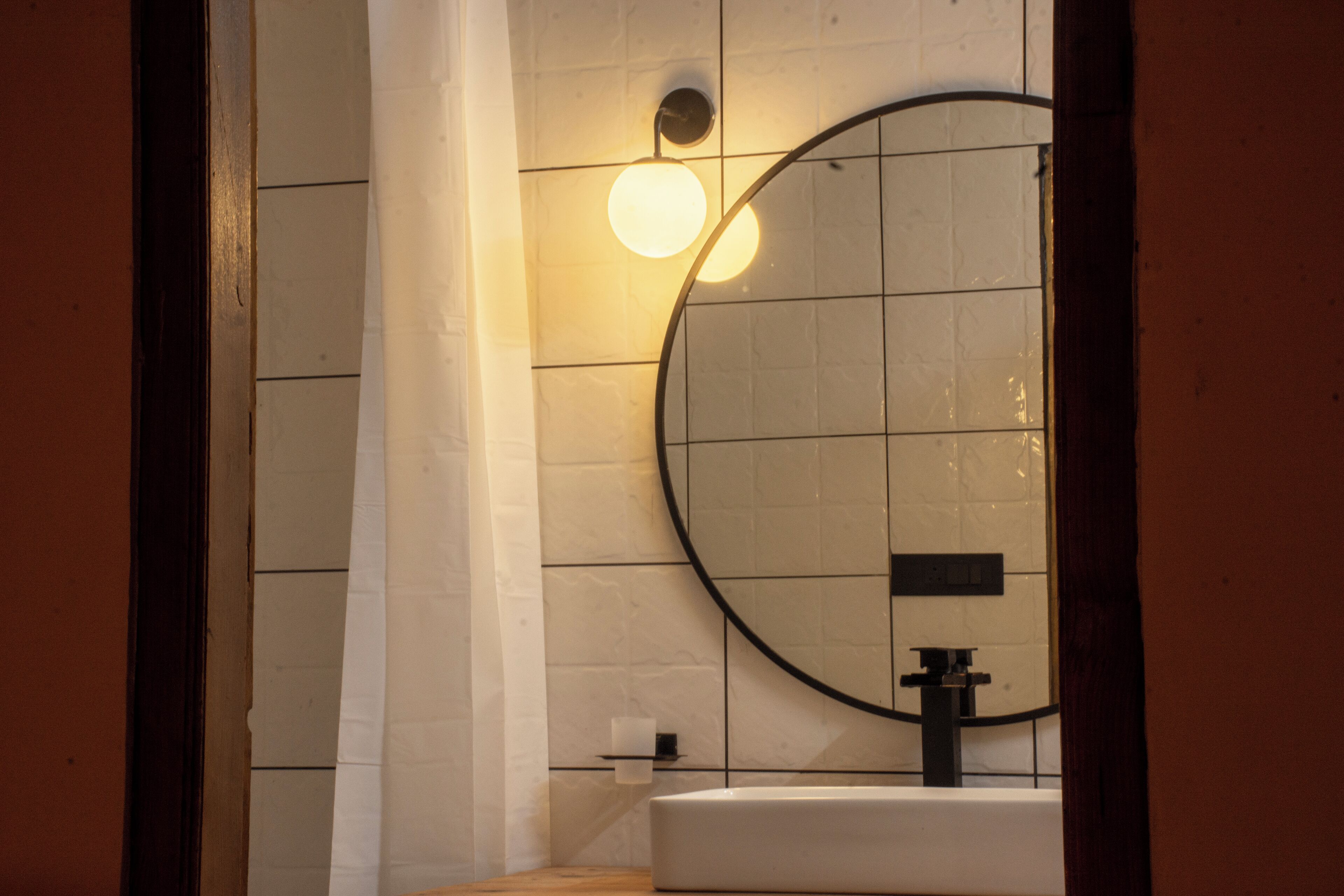 A bathroom with a round mirror, a white sink, and a wall-mounted light fixture.