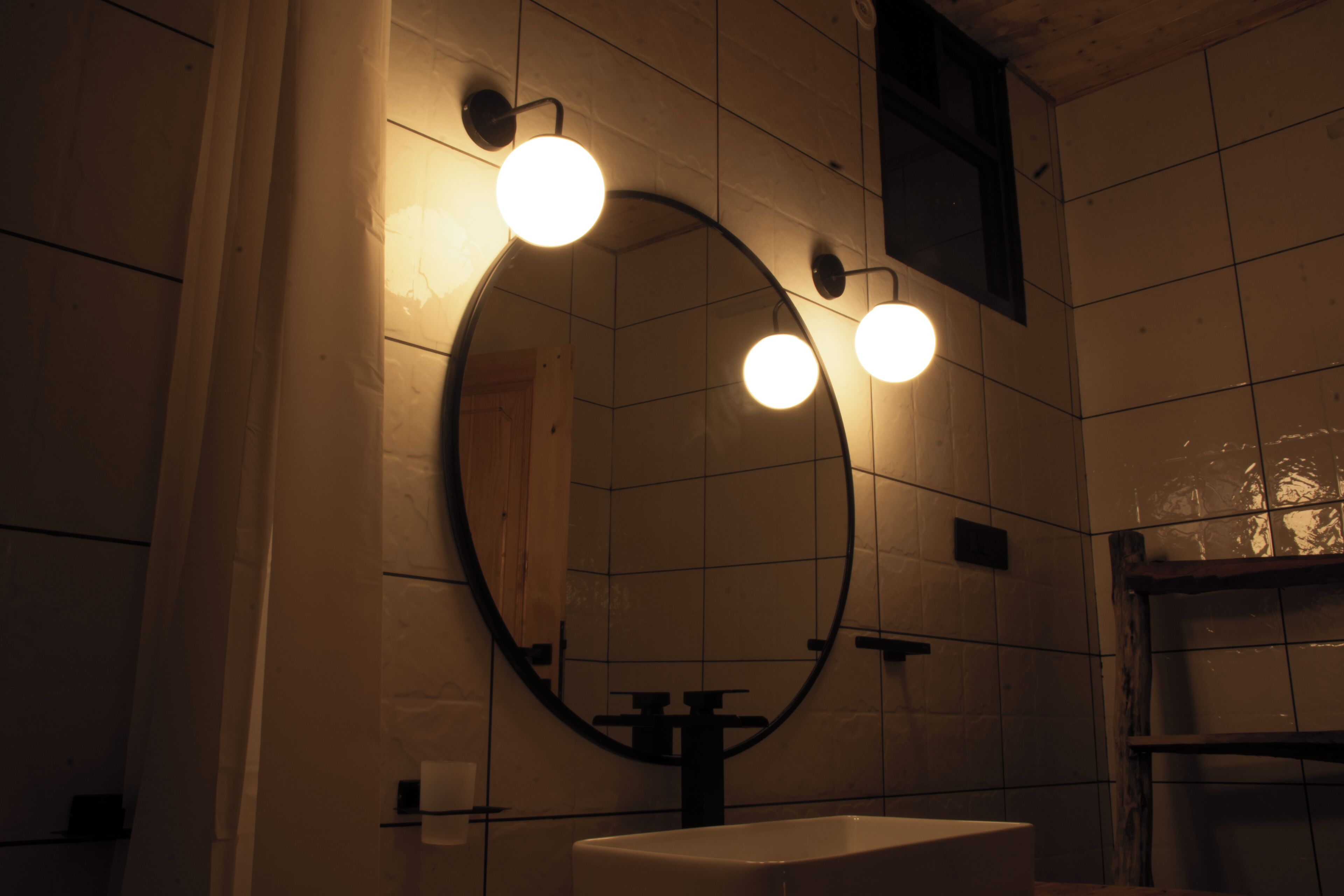 Ein Badezimmer mit rundem Spiegel, drei Wandleuchten und einem weißen Waschbecken.