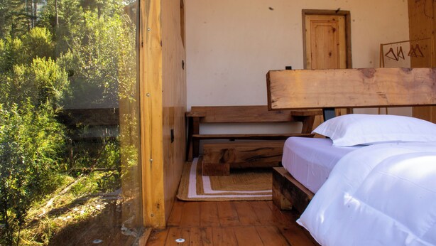 A wooden cabin with a single bed, a wooden bench, and a door. - Cove The Glass House (Manali)