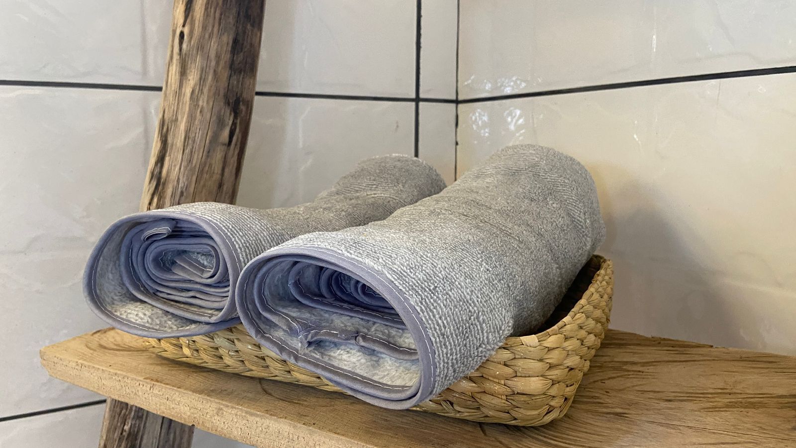 Two rolled-up towels placed on a woven basket on a wooden shelf.