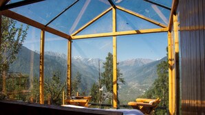 A wooden cabin with a glass ceiling, offering a mountain view. Inside, there are two wooden chairs and a bench. - Cove The Glass House (Manali)