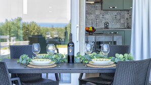 A dining table set with wine glasses, a bottle, and a bowl of fruit, with a view of the sea through a glass door. - Posidonia by Interhome (Valledoria)