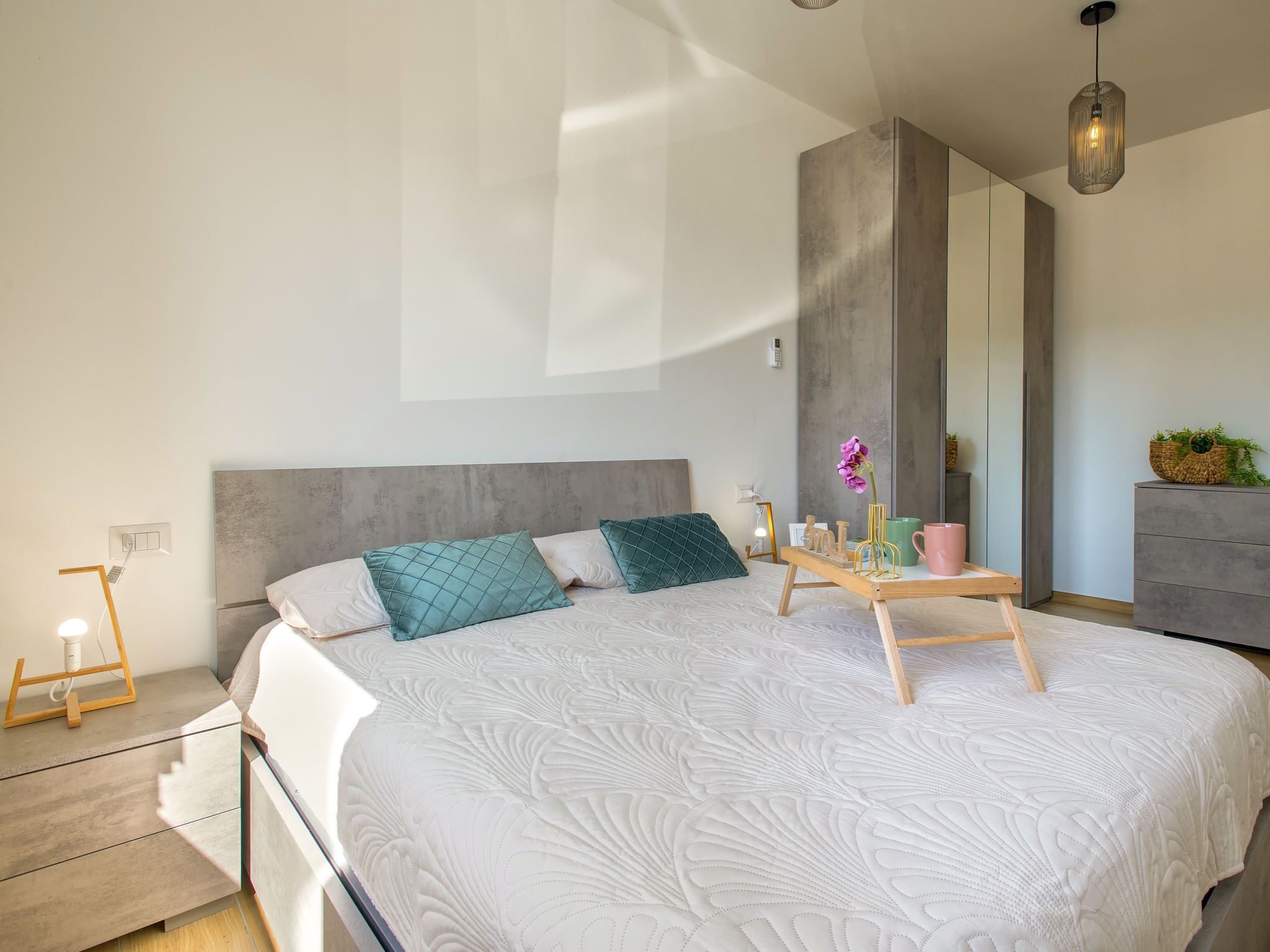 Une chambre à coucher moderne avec un grand lit, une table de chevet avec une lampe, une commode et un miroir.