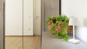 A hallway with a wooden floor, a woven basket with greenery, a white lamp, and a door. - Posidonia by Interhome (Valledoria)