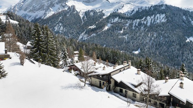 Un paysage montagneux enneigé avec une maison moderne dotée d’une grande fenêtre et d’une cheminée.