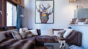Un salon chaleureux avec un grand tableau coloré représentant un cerf, encadré, un ensemble de canapés et une petite table sur laquelle est posée une figurine décorative de renne.