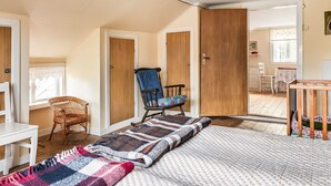A cozy bedroom with a large bed, a wooden door, a wicker chair, and a small table with a chair. - Mjuamåla by Interhome (Eringsboda)