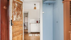 A hallway with a rustic wooden door, a white kitchen with a refrigerator, and a blue wall. - Mjuamåla by Interhome (Eringsboda)
