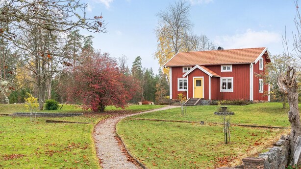 A red house with a yellow door, surrounded by a stone wall and a grassy area with a winding path. - Mjuamåla by Interhome (Eringsboda)