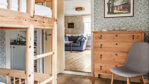 A room with a bunk bed, wooden dresser, and a chair. There is a door leading to another room with a sofa and a table. - Mjuamåla by Interhome (Eringsboda)