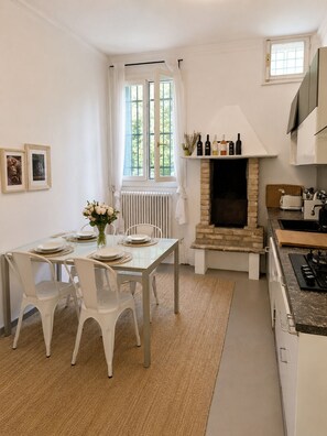 A modern kitchen with a stone fireplace, white cabinetry, and a dining area with white chairs and a table set for four.