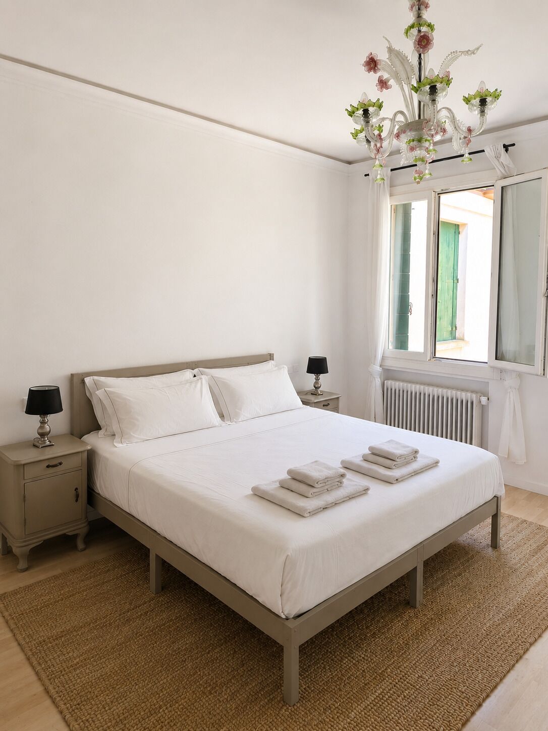 Een slaapkamer met een bed, nachtkastjes, een kroonluchter, een raam met gordijnen en een radiator.