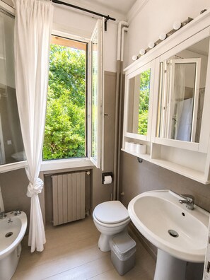 Een badkamer met toilet, wastafel en raam met gordijnen.