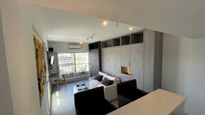 A modern living room with a white sofa, a black chair, and a coffee table. There is a large window with a view of buildings outside. - Fantastic Studio With Balcony Pool (Buenos Aires)